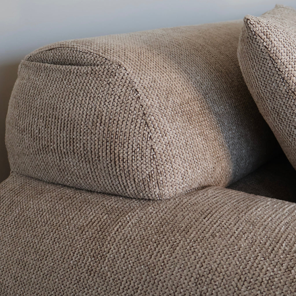 Close-up of a textured beige upholstered sofa cushion and matching pillow against a plain light wall.