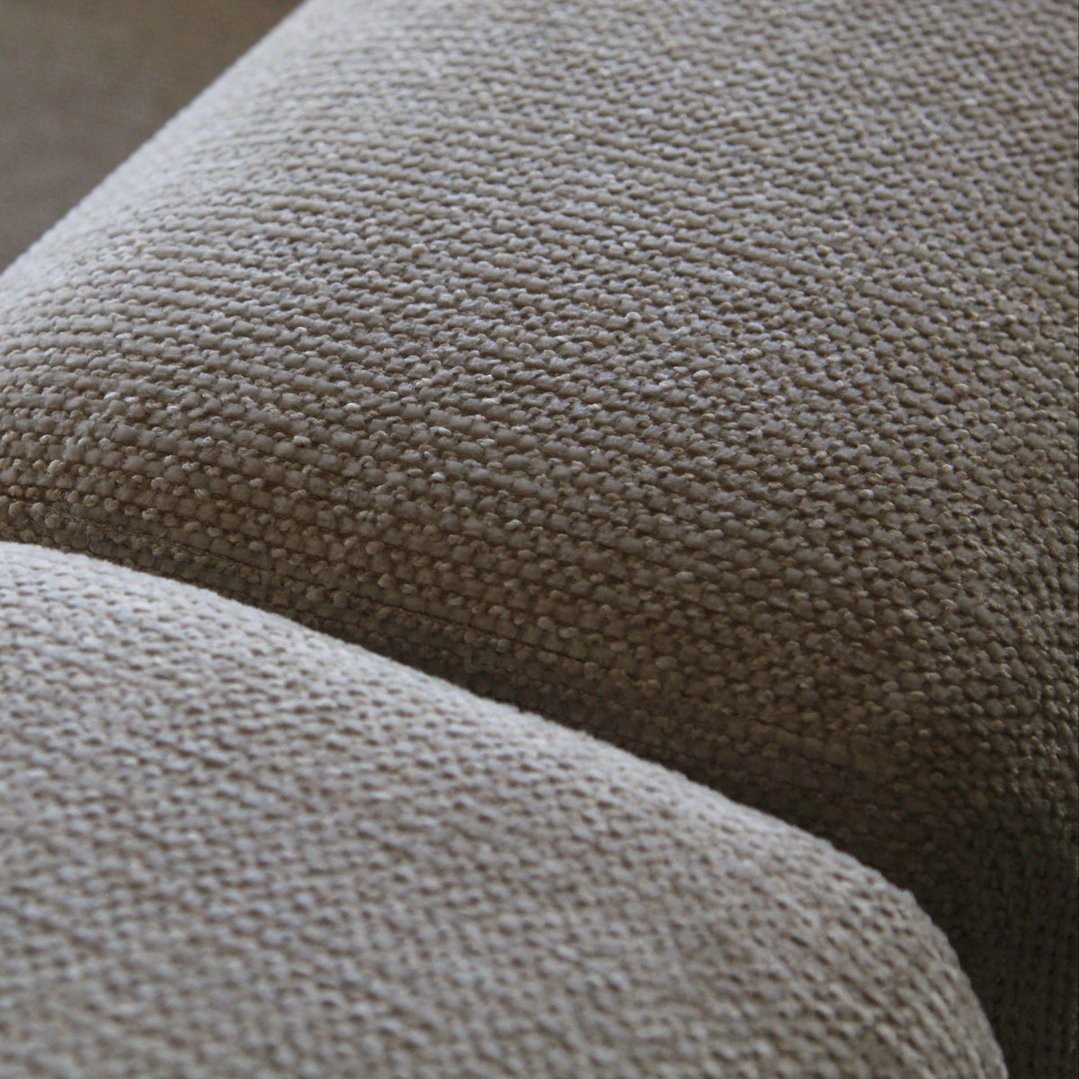 Close-up of a textured woven fabric upholstery in a warm taupe-beige color, showing the detailed weave and curved contours of what appears to be a sofa or cushion.