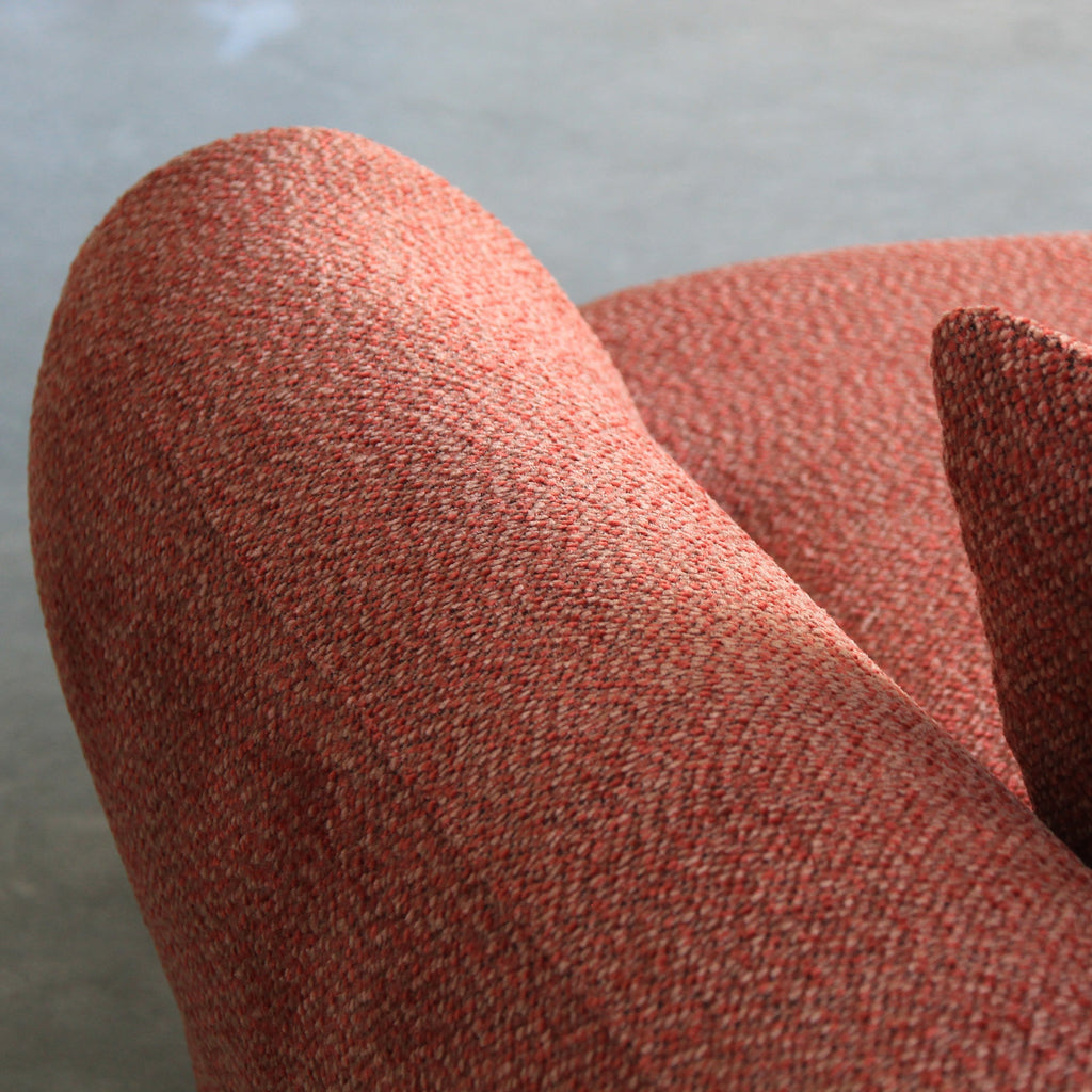 Close-up of a textured terracotta orange upholstered chair with matching accent pillows, set against a neutral gray concrete floor.